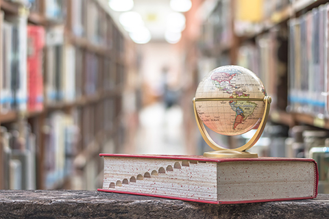 This is a stock image from Shutter stock. The photo was taken in a library. The subject of the photo is a globe placed on top of an encyclopedia. The background is blurred.