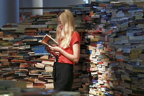 A stock photo of a woman reading a book among a pile of books.
